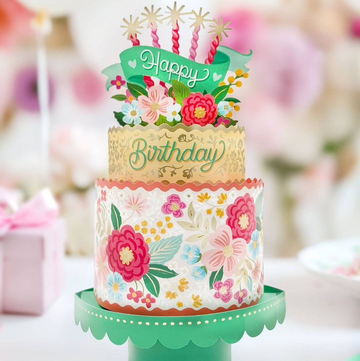 Decorative birthday cake with floral design and 'Happy Birthday' topper on a green stand.