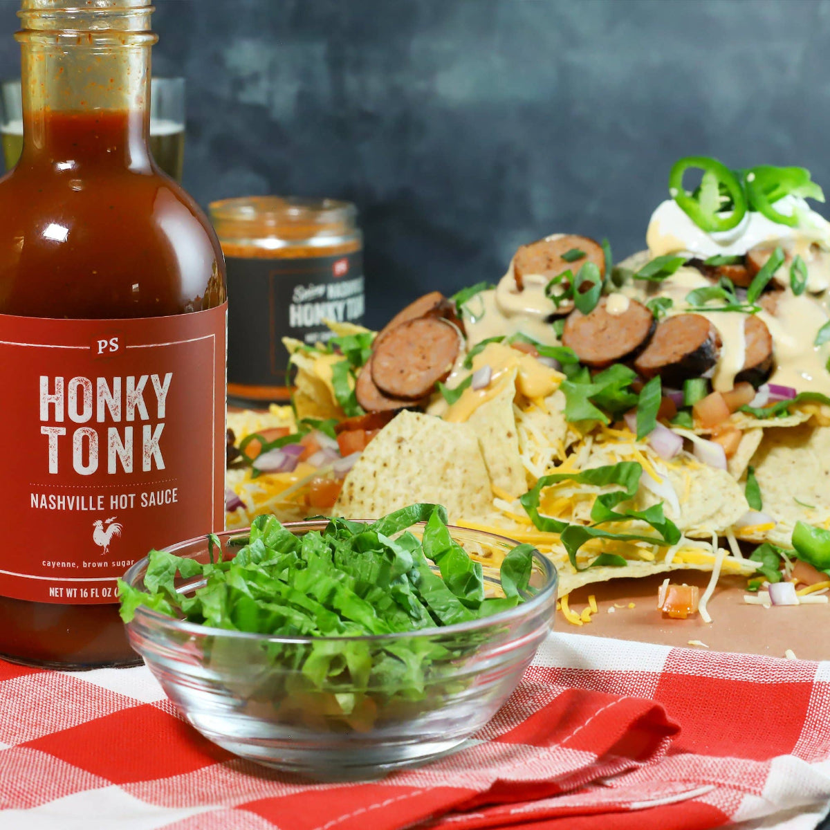 PS Honky Tonk Nashville hot sauce bottle with nachos and greens on a checkered tablecloth.