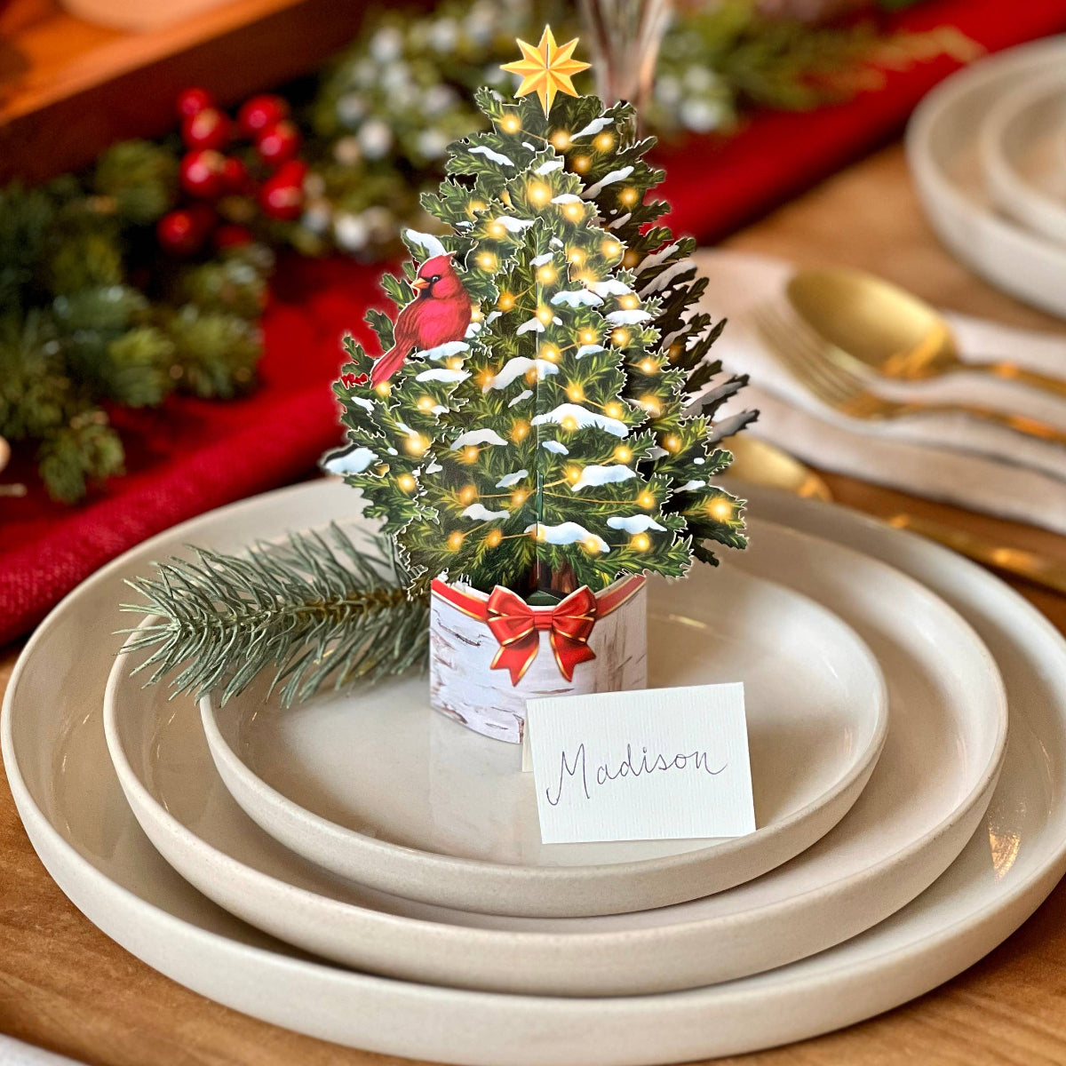 Decorative Christmas tree on a place setting with candles and greenery in the background.