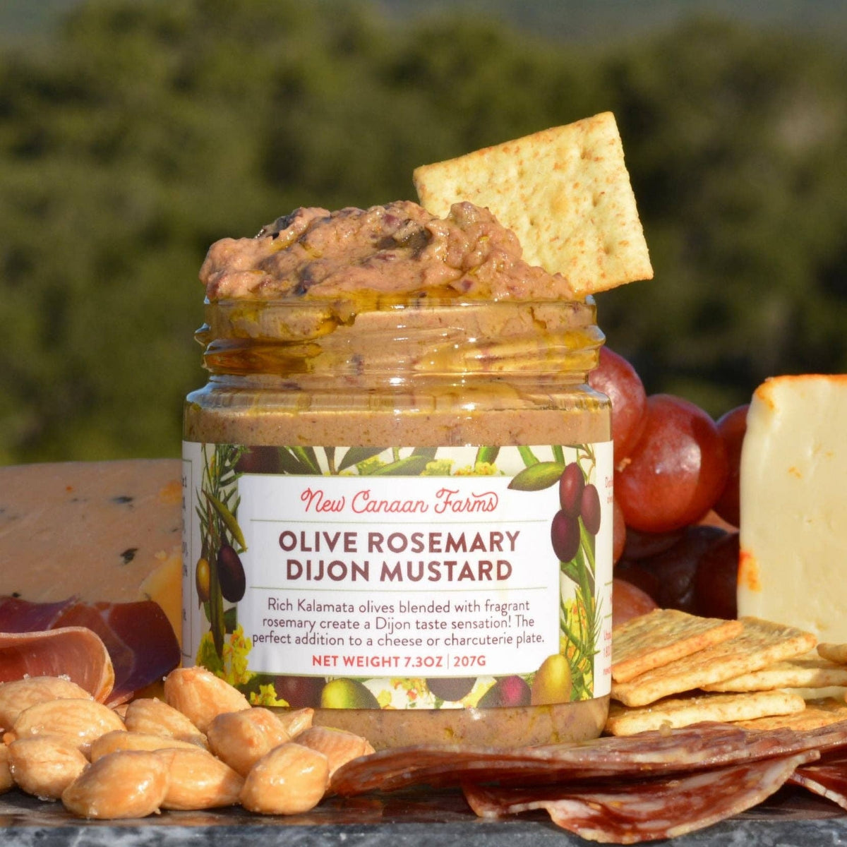 Jar of olive rosemary dijon mustard on a charcuterie board with crackers and cheese.