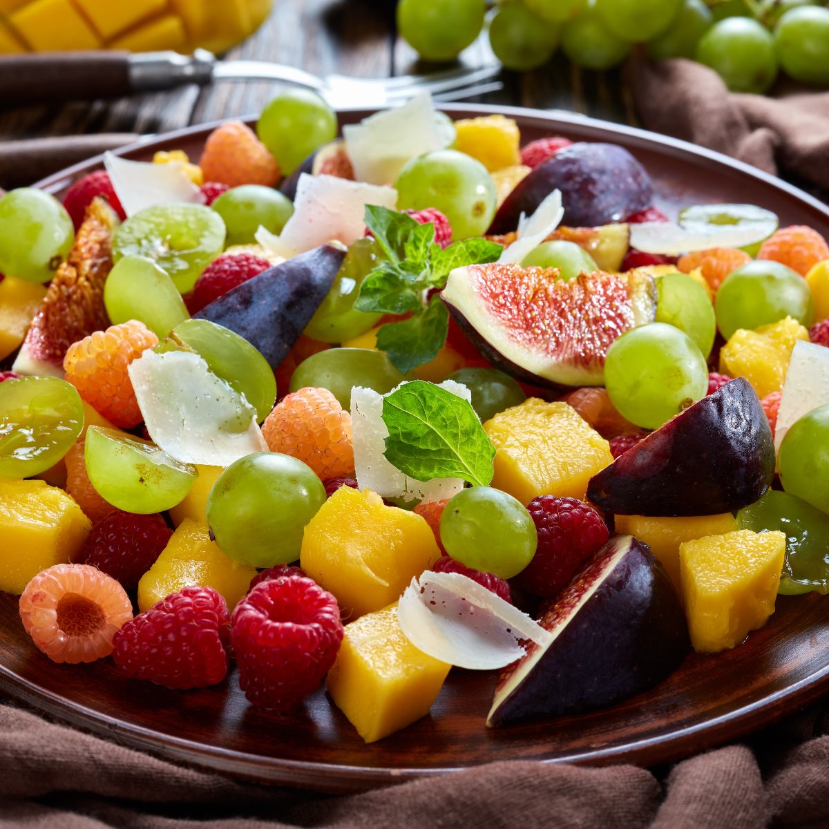 Assorted fruit salad on a wooden plate with a brown napkin underneath.