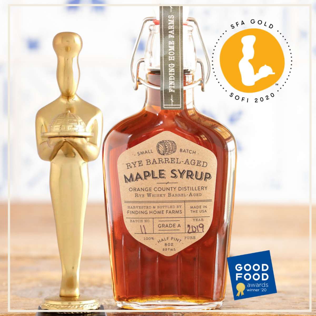 Bottle of Rye Barrel-Aged Maple Syrup with an Oscar statue and Good Food Award badge on a light background