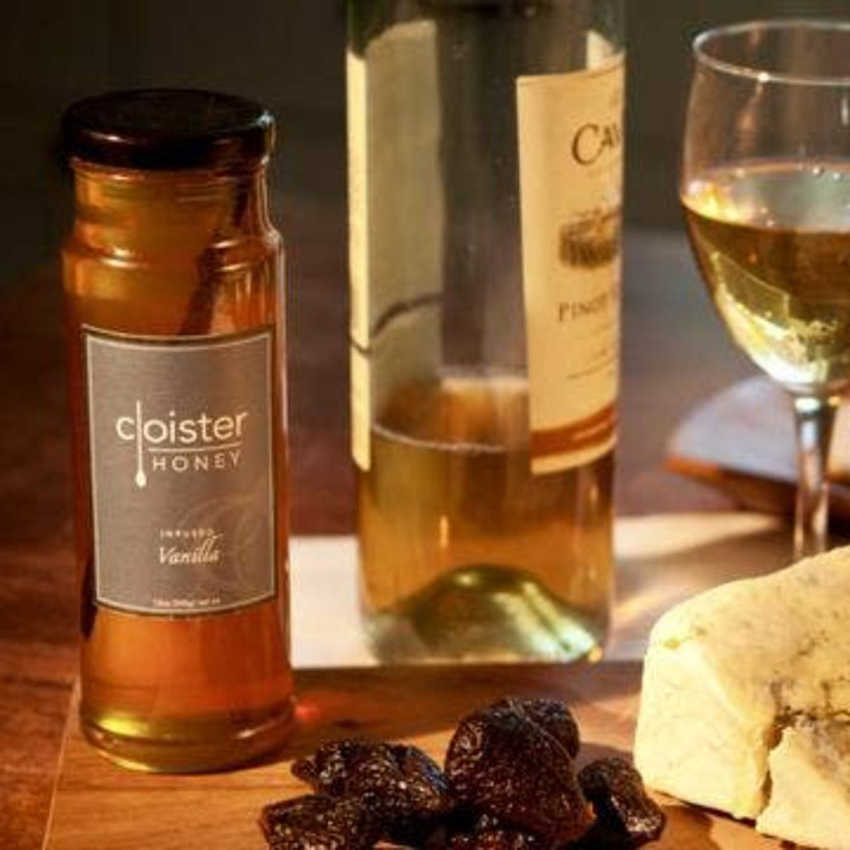 Cloister honey, a bottle of wine, a glass of wine, dried fruits, and cheese on a wooden board.