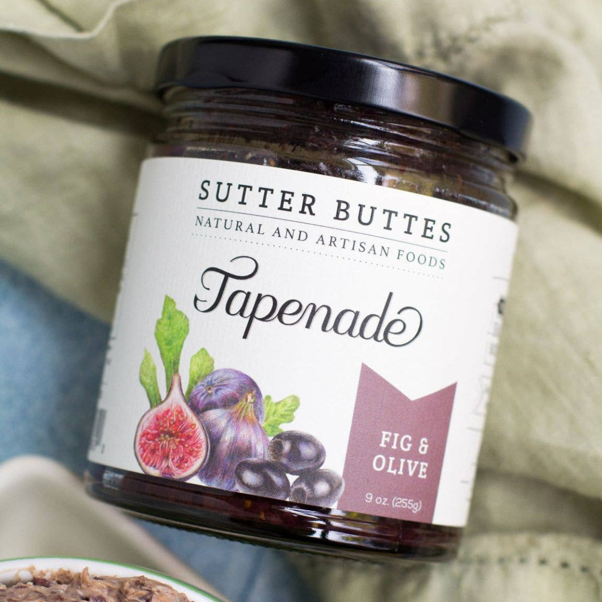 Jar of Sutter Buttes Fig & Olive Tapenade on a textured fabric background