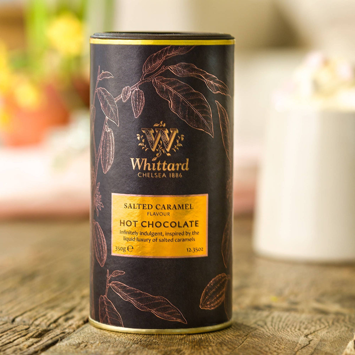 Whittard salted caramel hot chocolate canister on a wooden surface with blurred background