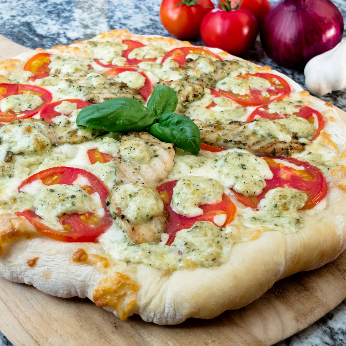 Pizza with tomatoes and basil on a wooden board with ingredients in the background