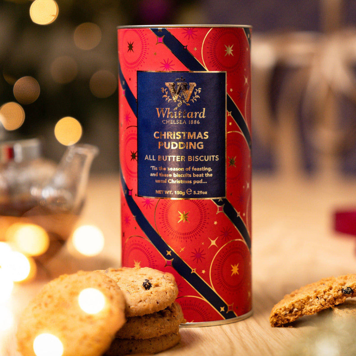 Red can of Whitfield Christmas Pudding biscuits with blurred lights in the background