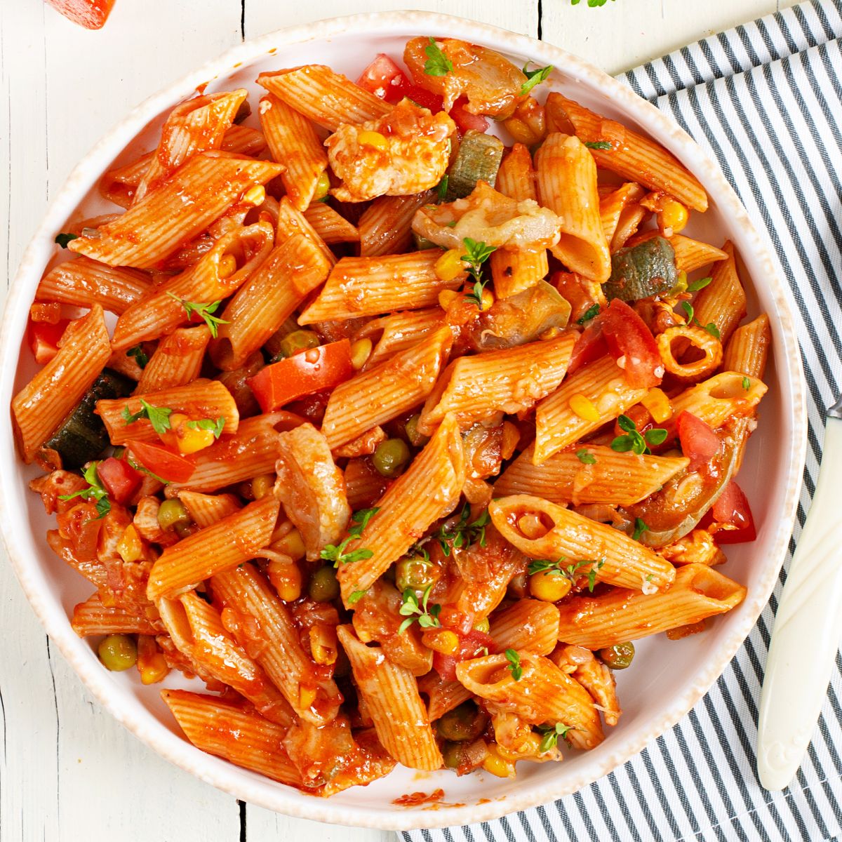 Penne pasta with chicken and vegetables in a red sauce in a white bowl.