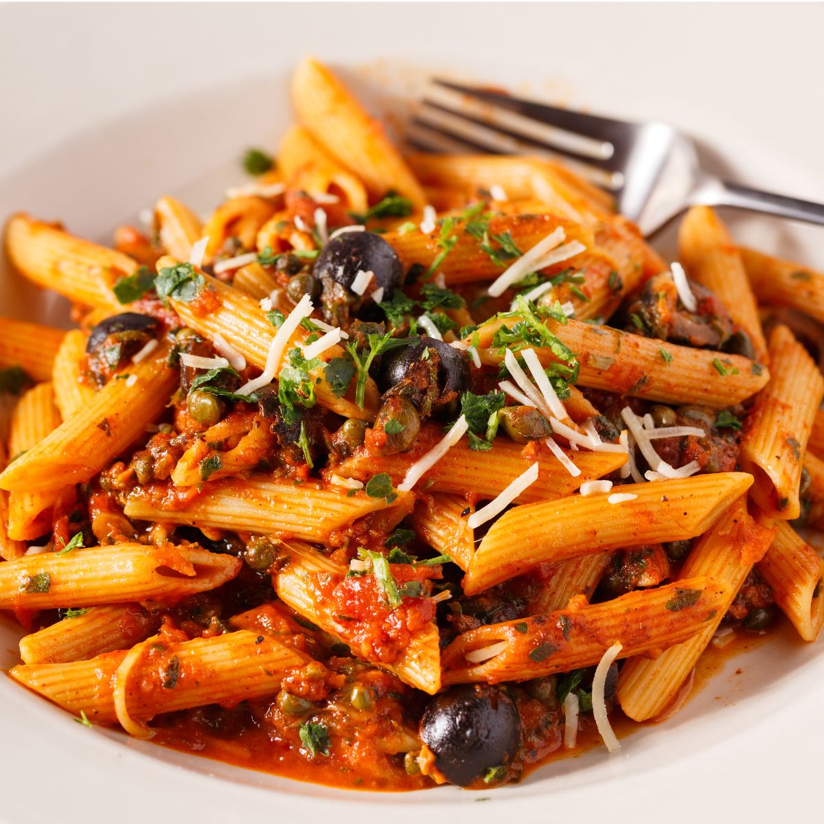 Penne pasta with tomato sauce, olives, and herbs on a white plate with a fork.