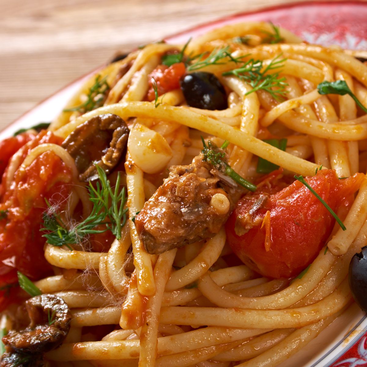 Spaghetti dish with tomatoes, olives, and herbs on a plate