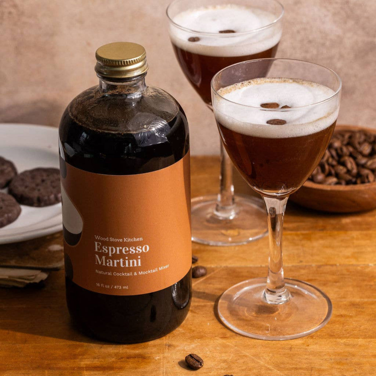 Bottle of Espresso Martini mixer with two glasses on a wooden table.