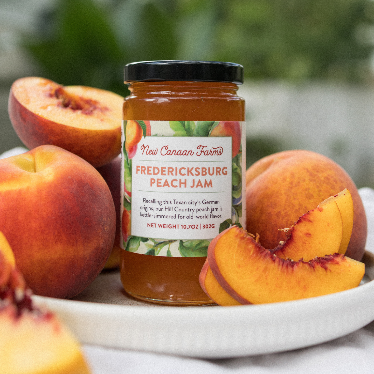 Jar of Fredericksburg Peach Jam with peaches on a plate outdoors