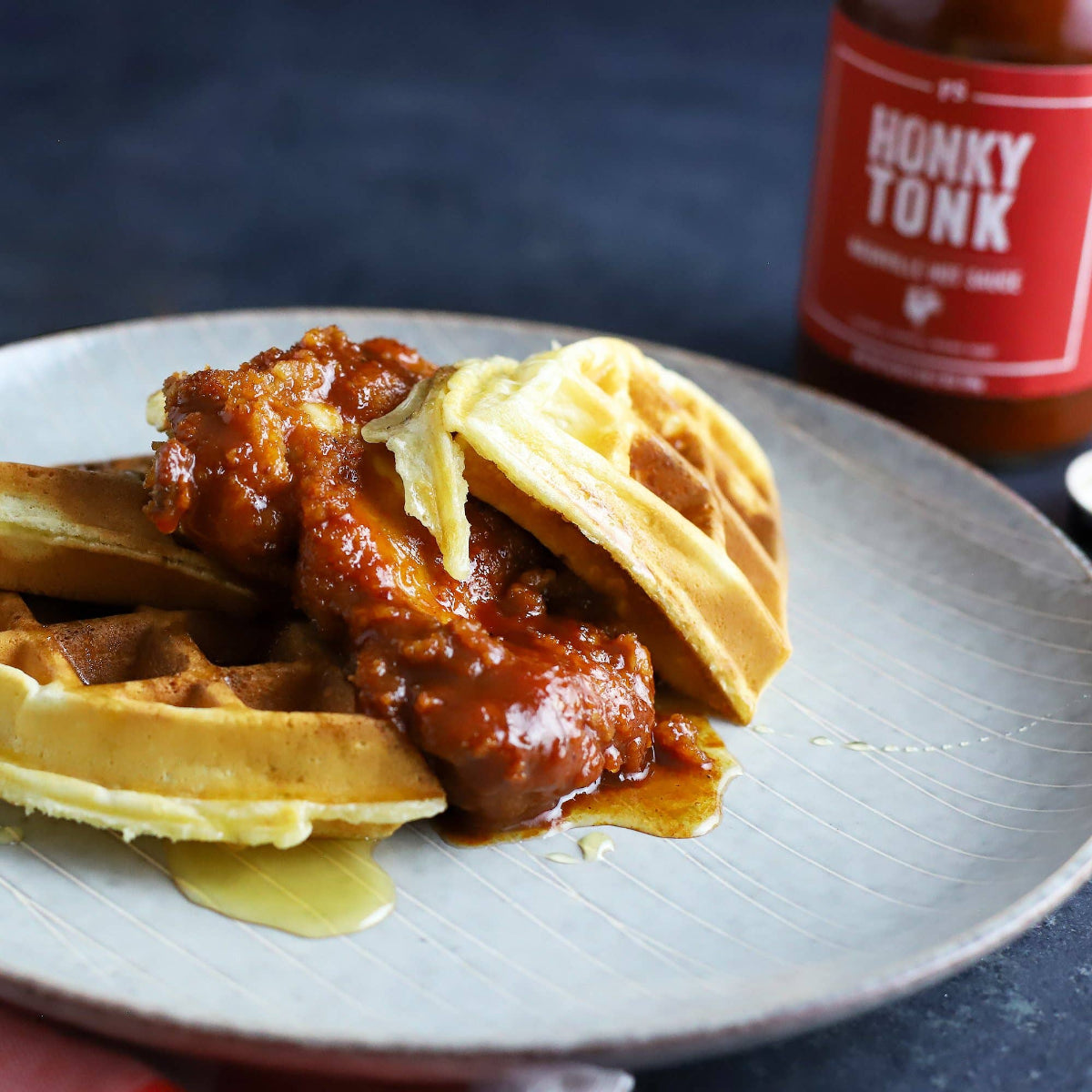 Plate of chicken and waffles with a bottle of 'Honky Tonk' hot sauce in the background.