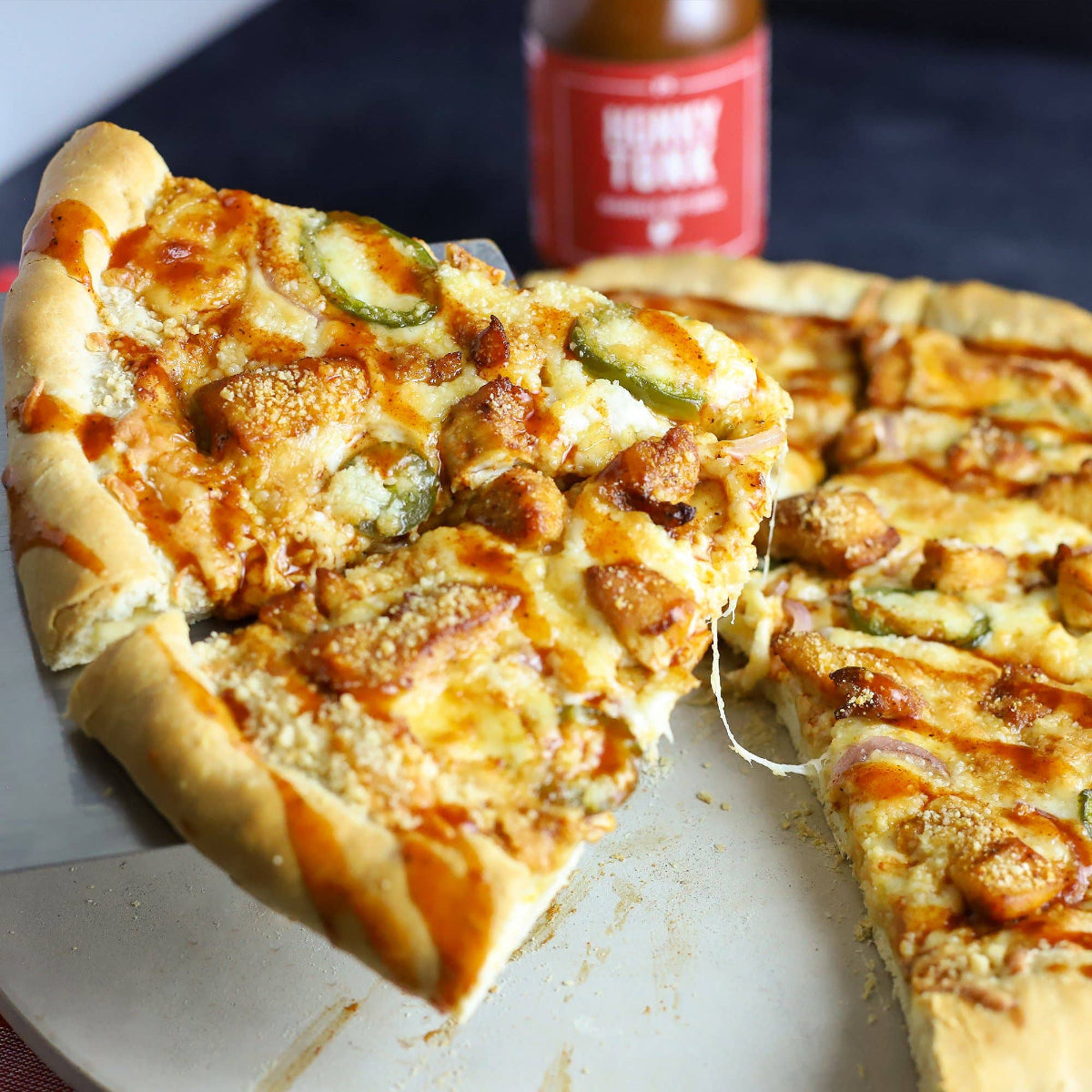 Slice of pizza with chicken and jalapeños on a pan with a bottle in the background