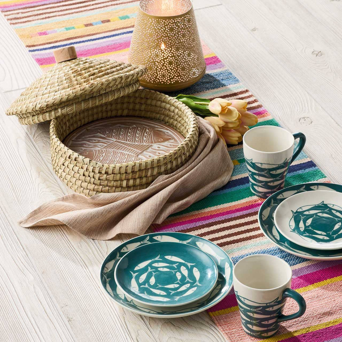 Table setting with ceramic plates and cups on a colorful striped tablecloth.