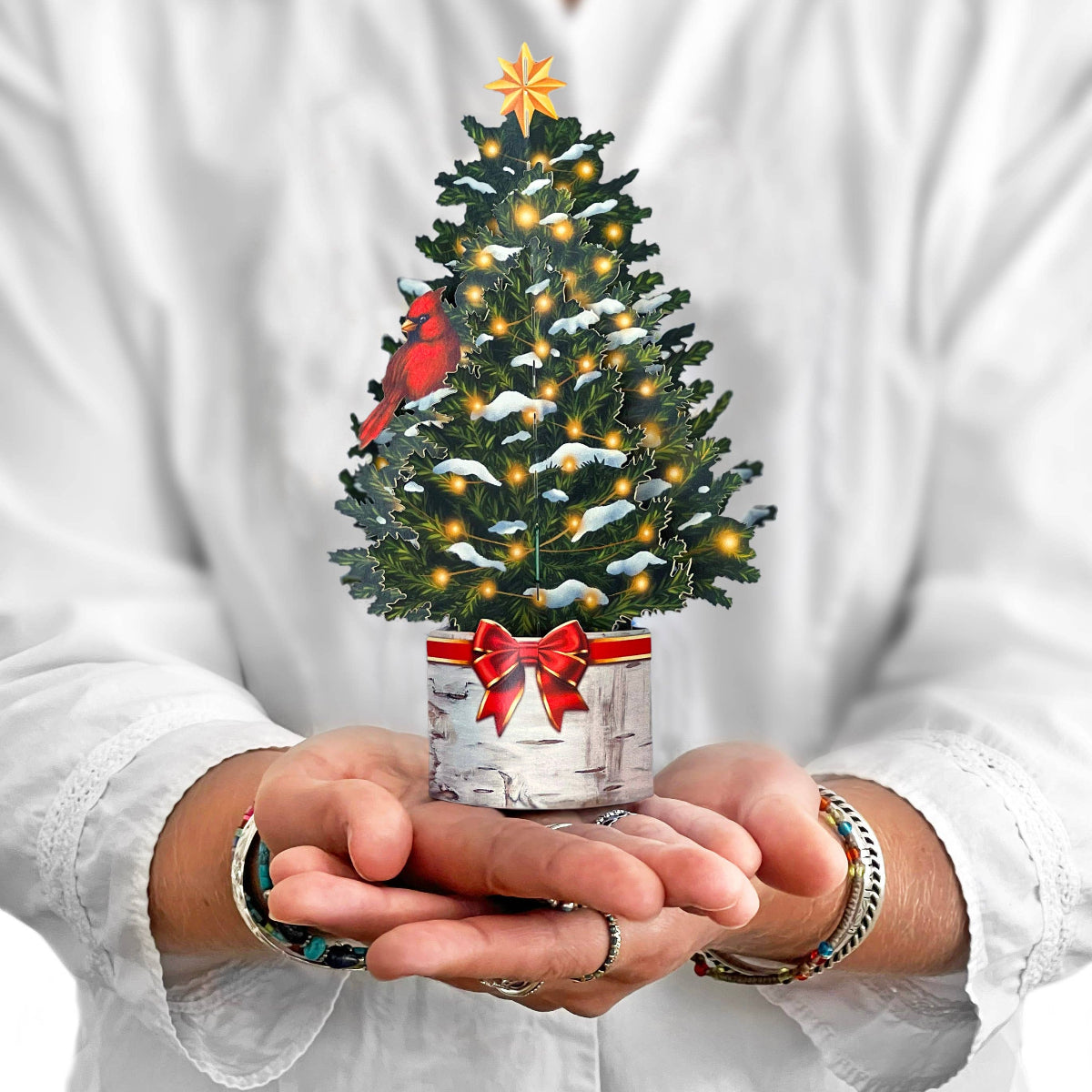 Person holding a small decorated Christmas tree with lights and a red bow.