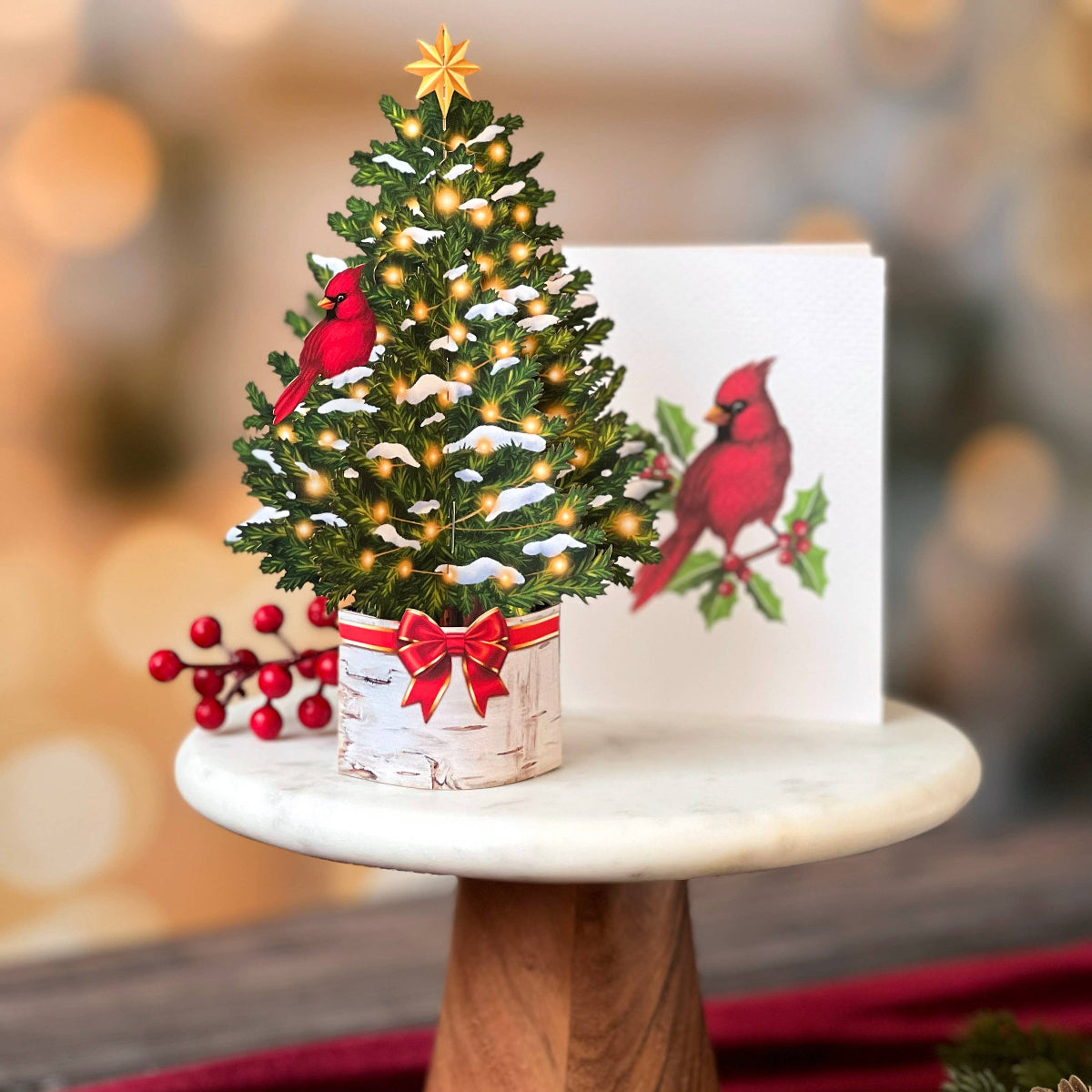 Small Christmas tree with lights and red cardinal decorations on a wooden stand with a blurred background.