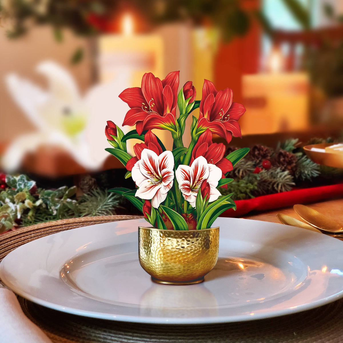 Decorative floral arrangement in a gold pot on a table setting with candles and greenery.