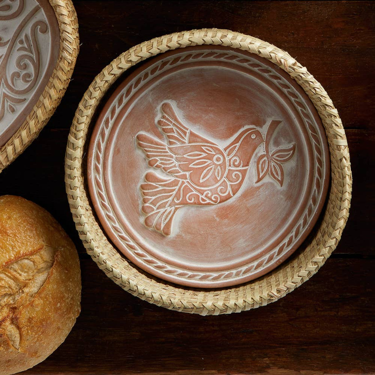 Ceramic plate with bird design on a woven lid, next to bread on a wooden surface