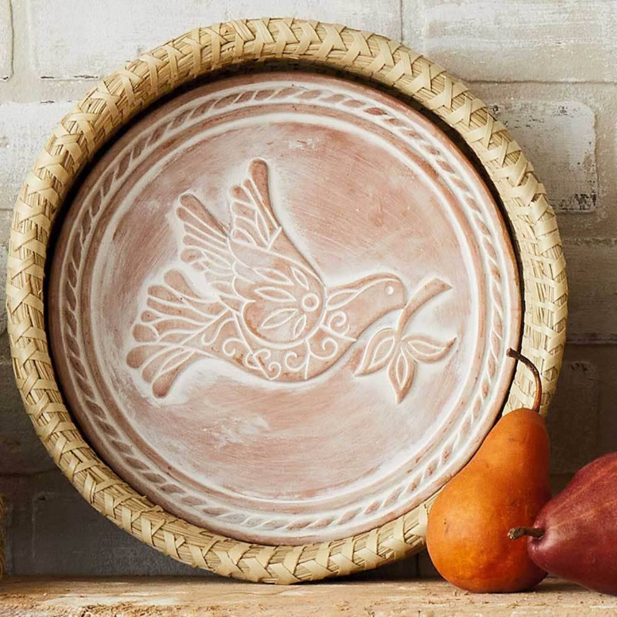 Decorative plate with bird design on a woven tray, placed on a wooden surface with gourds.