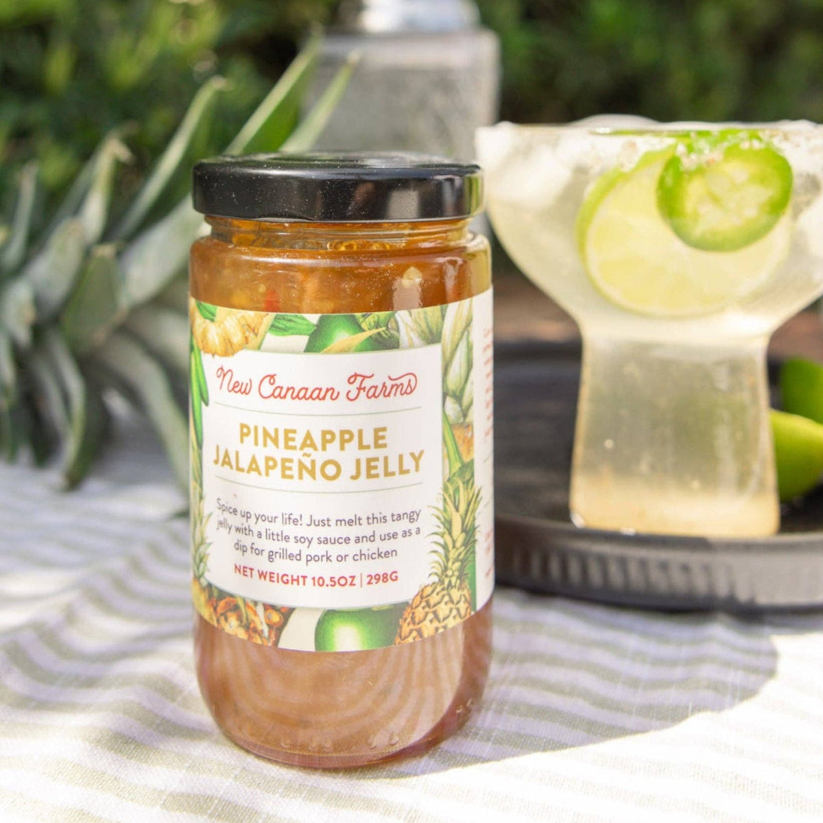 Jar of Pineapple Jalapeno Jelly on a table with a cocktail in the background