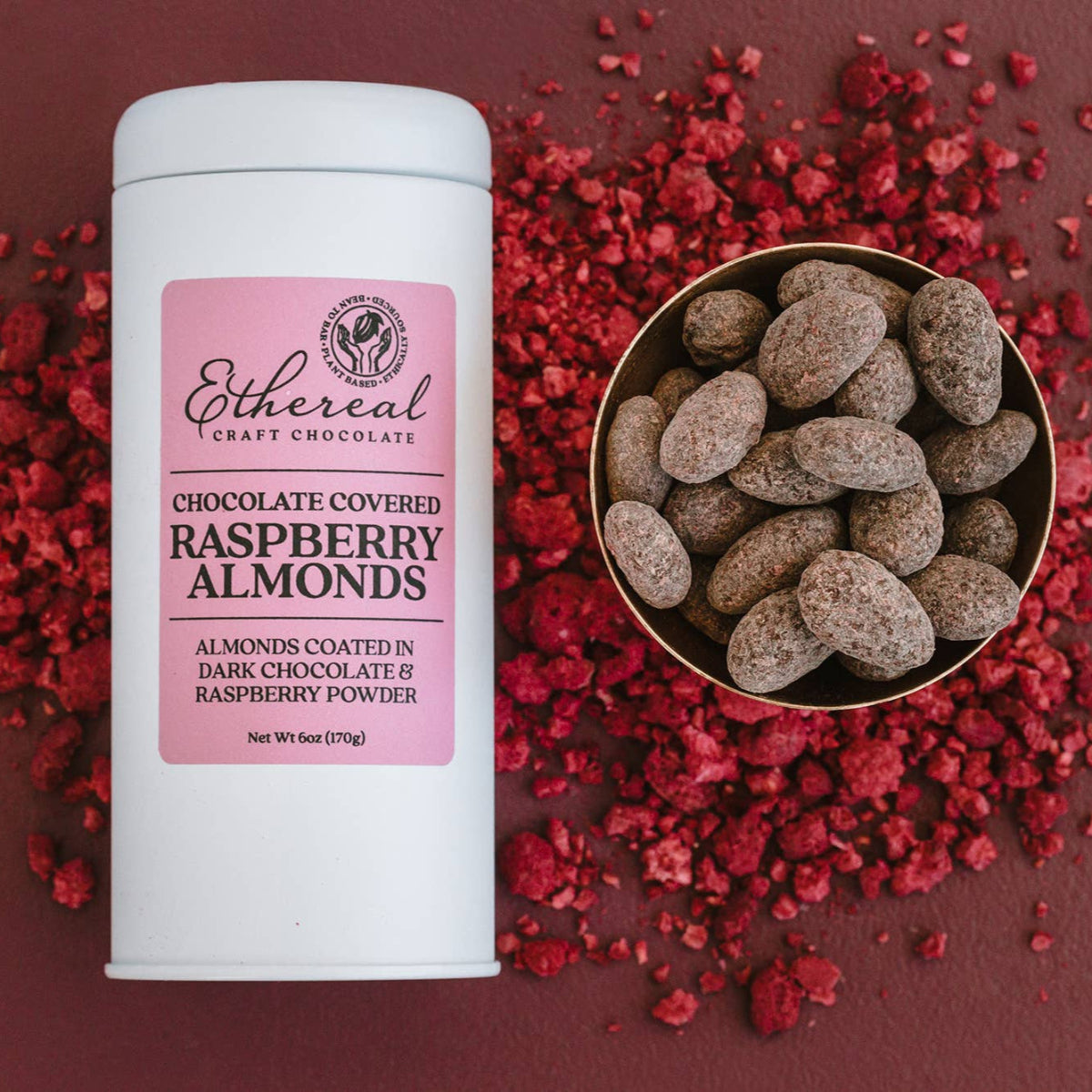 Container of Ethereal Craft Chocolates Raspberry Almonds on a red background with scattered raspberry pieces.