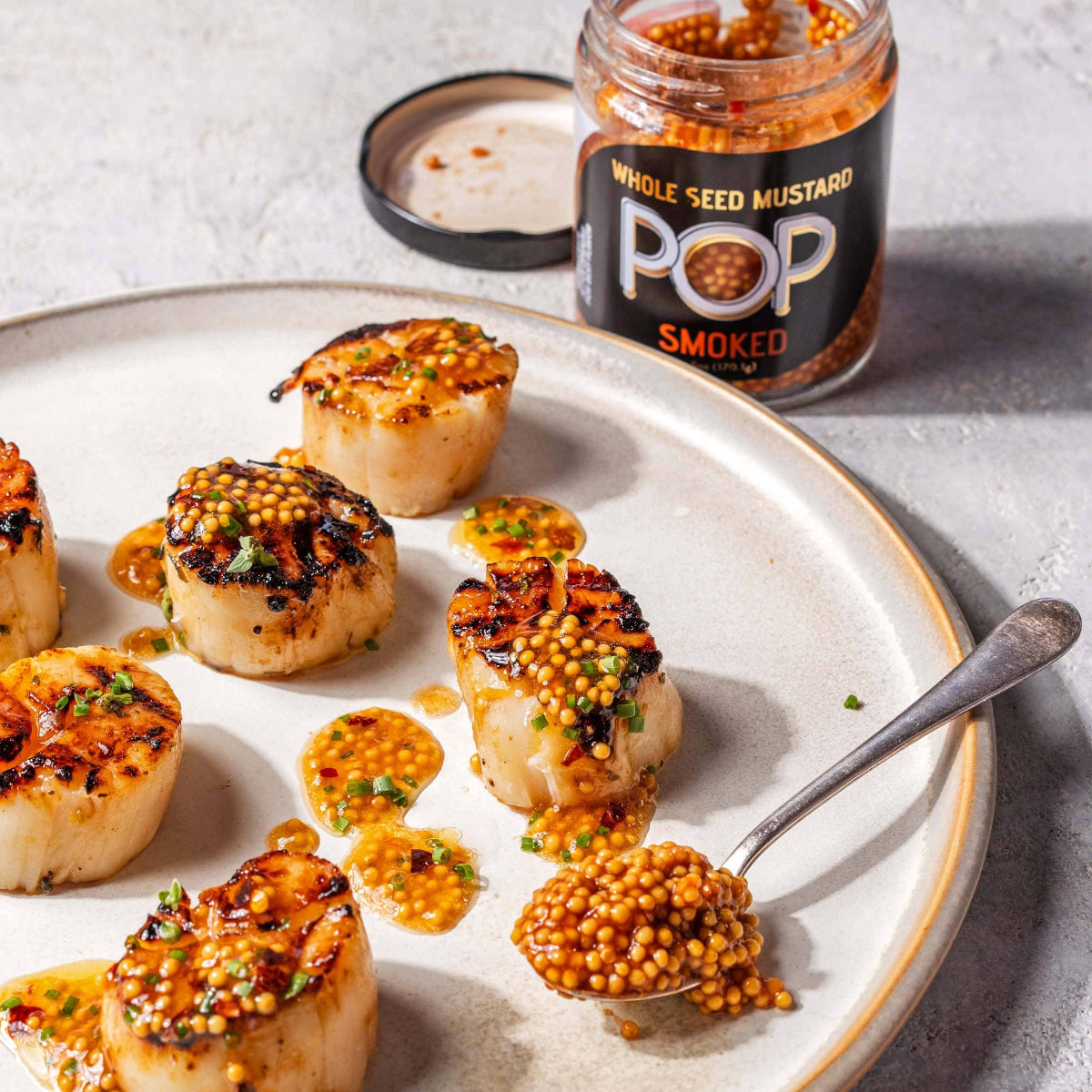 Scallops with mustard sauce on a plate with a jar of Pop Whole Seed Mustard.