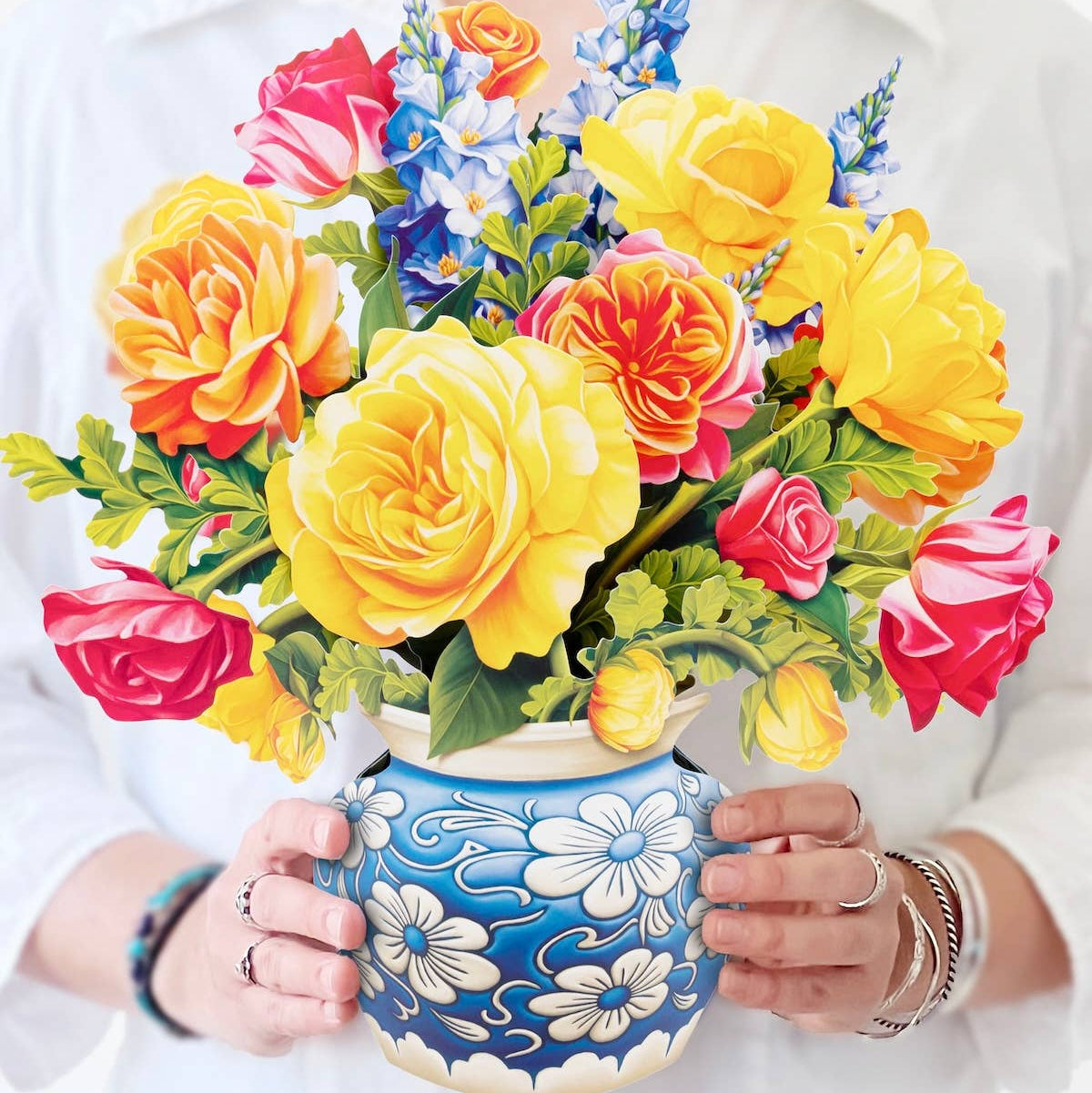 Person holding a colorful bouquet of flowers in a decorative blue vase.