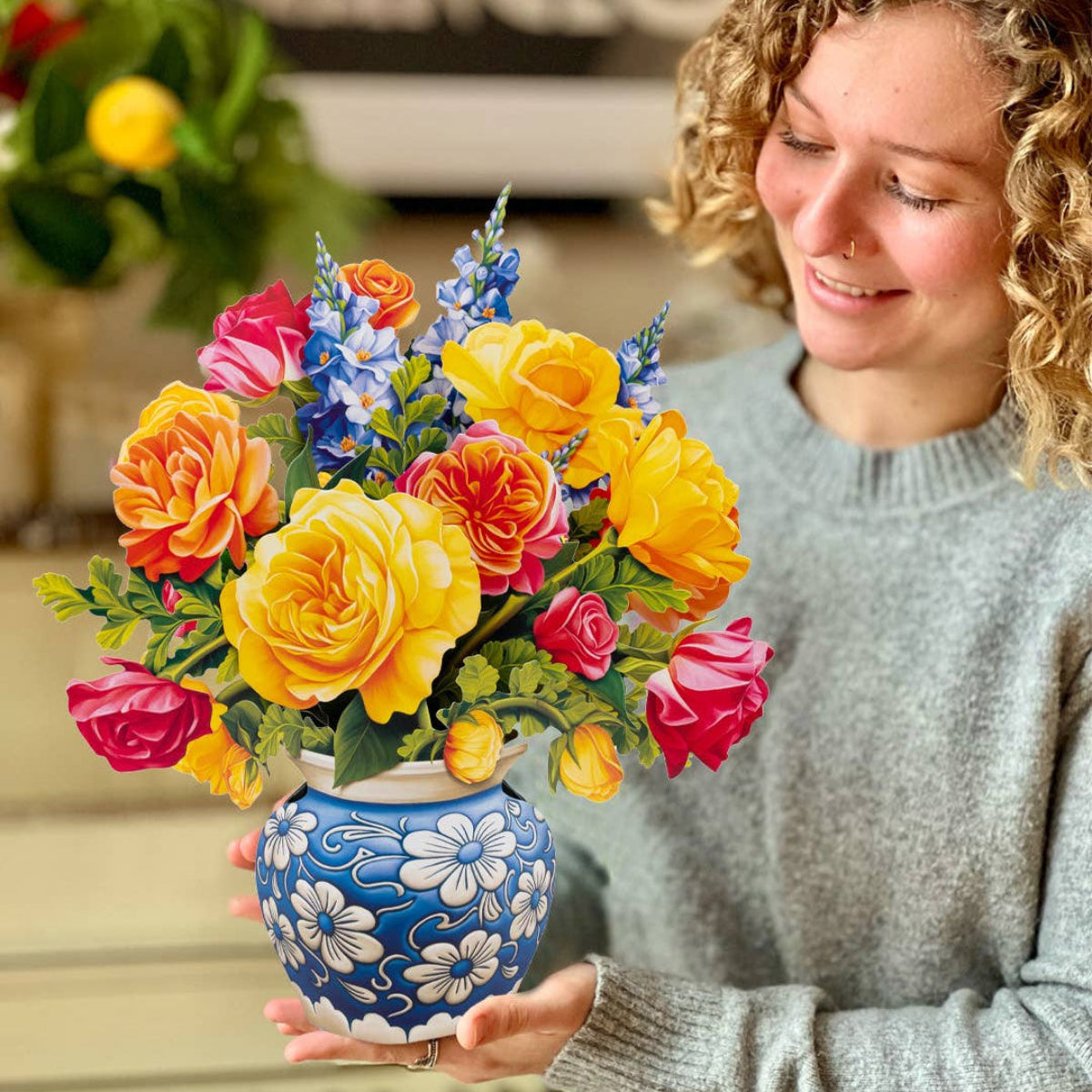 Woman holding a colorful bouquet of flowers in a blue vase, with a blurred background.