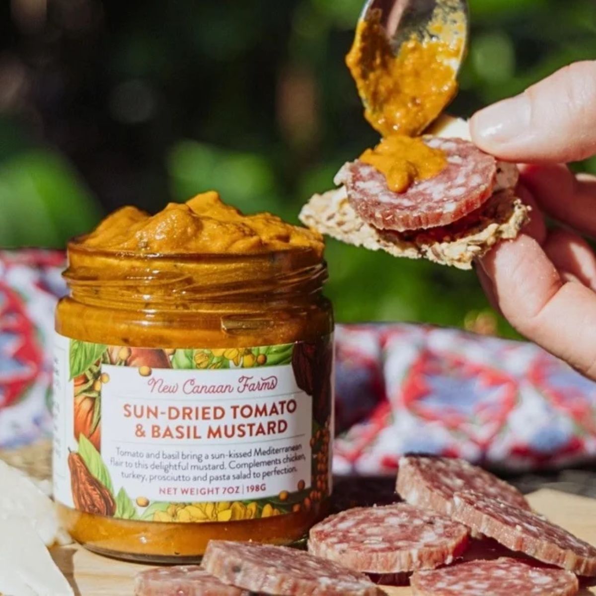 a person spreading mustard on a piece of meat and cracker