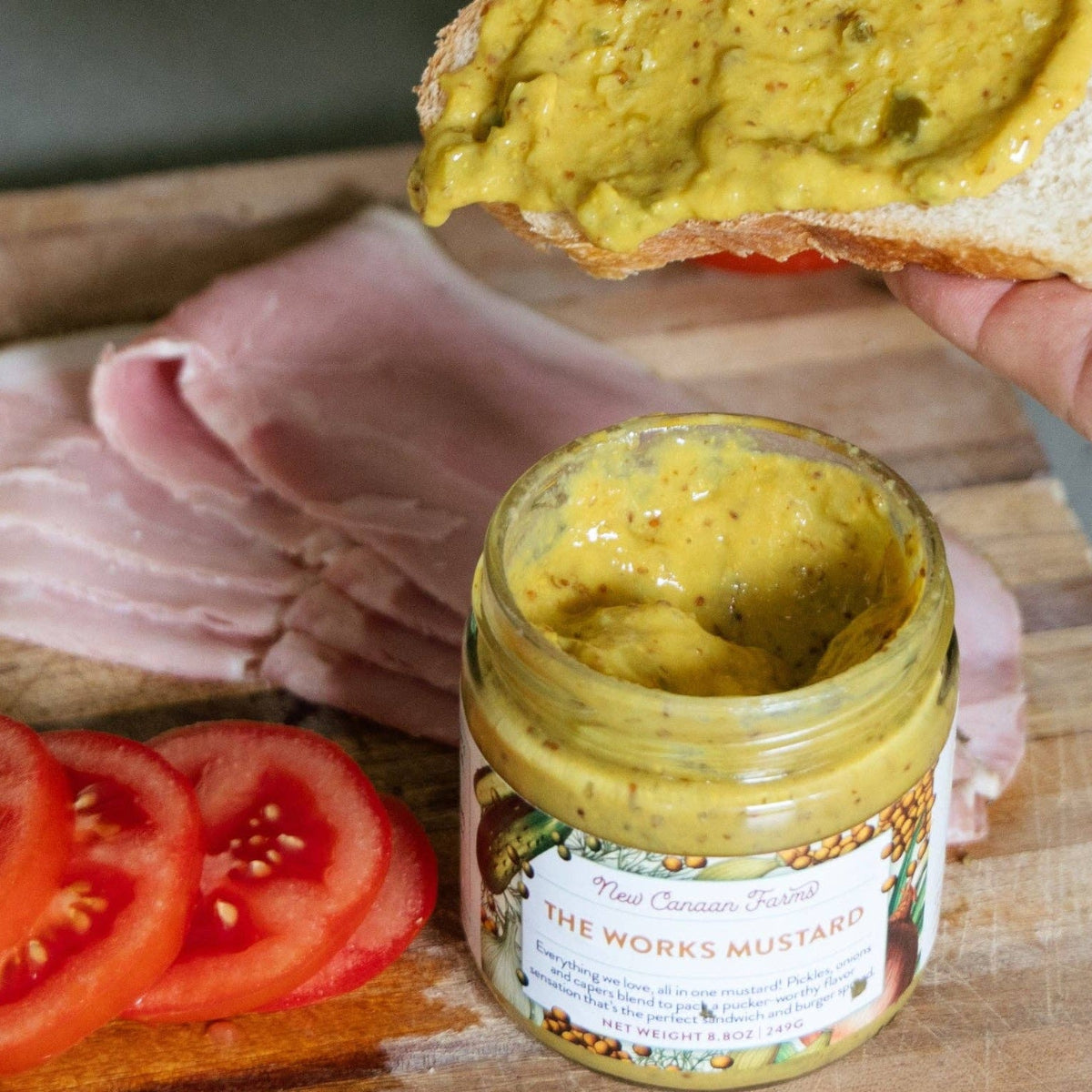 Mustard spread on bread with a jar of mustard and ingredients on a wooden board