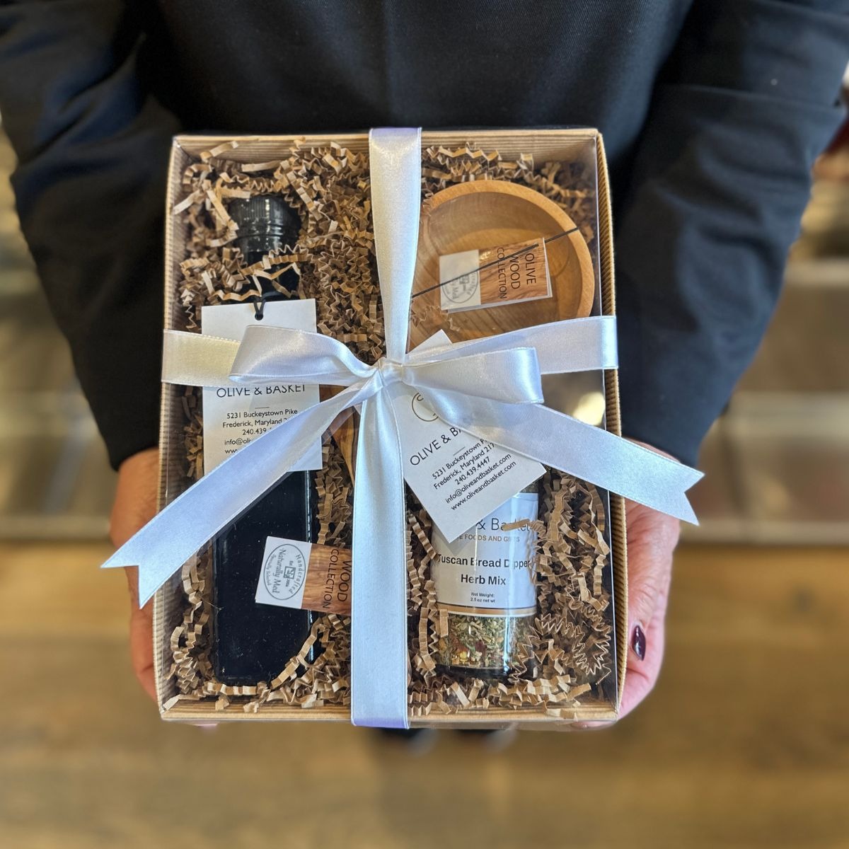 Gift box with a white ribbon held by a person, containing items from Olive & Oak.