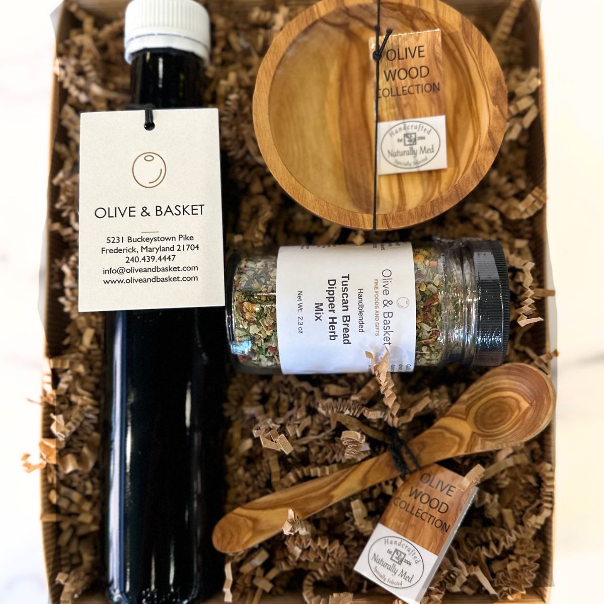 Gift set with olive oil, wooden spoon, and other items in a box labeled 'Olive & Basket'.