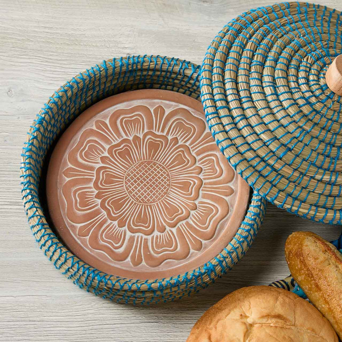 terra cotta dish lid with floral design inside a woven basket on a wooden surface