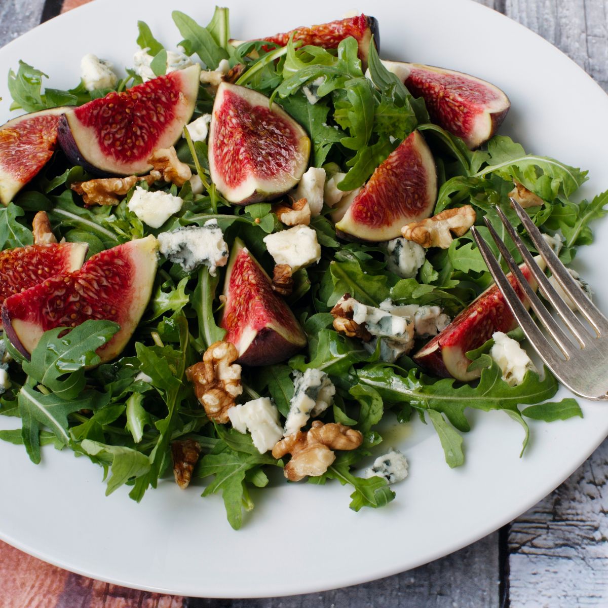 Salad with figs, arugula, and walnuts on a white plate with a fork.