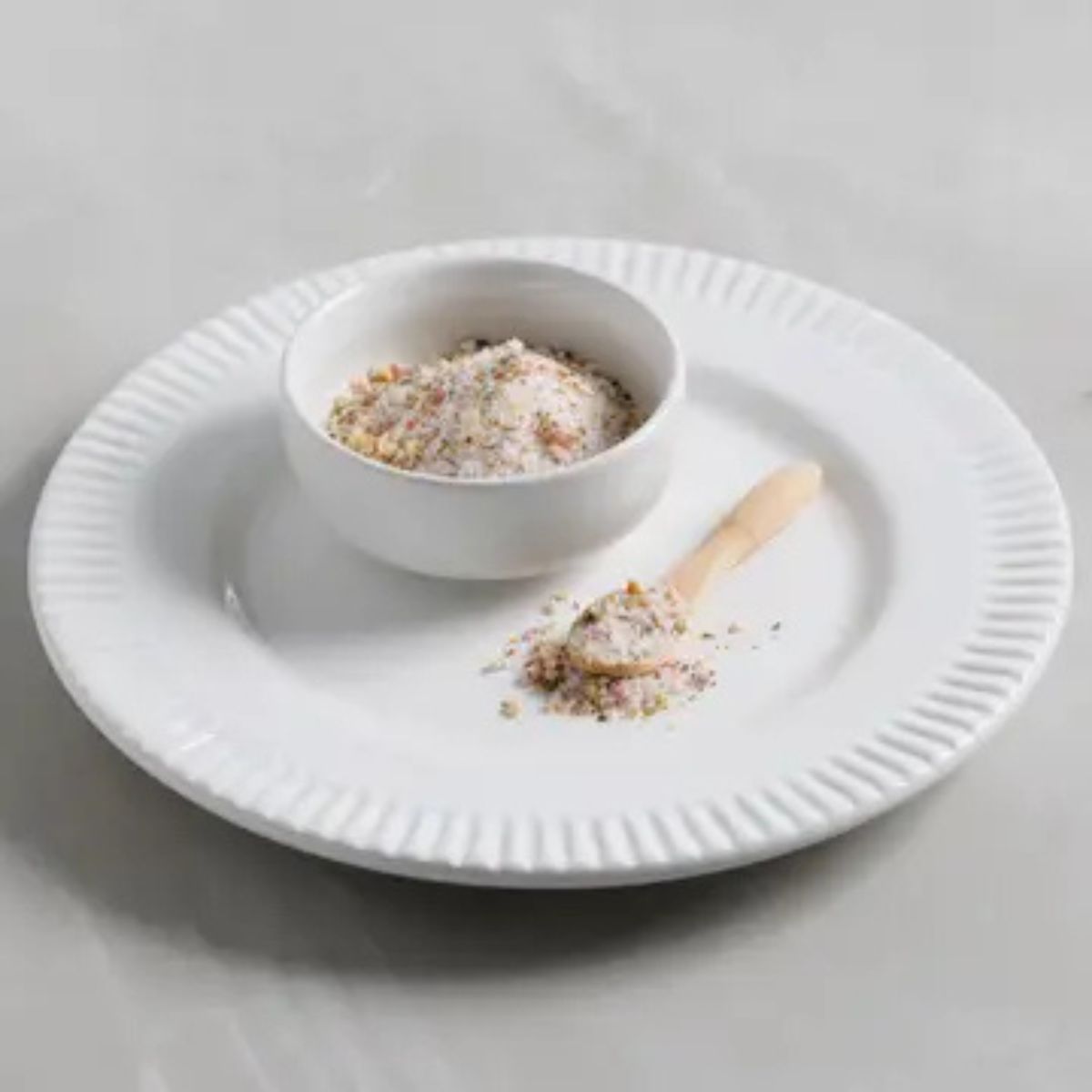 White plate with a bowl of salt and a wooden spoon on a light gray background