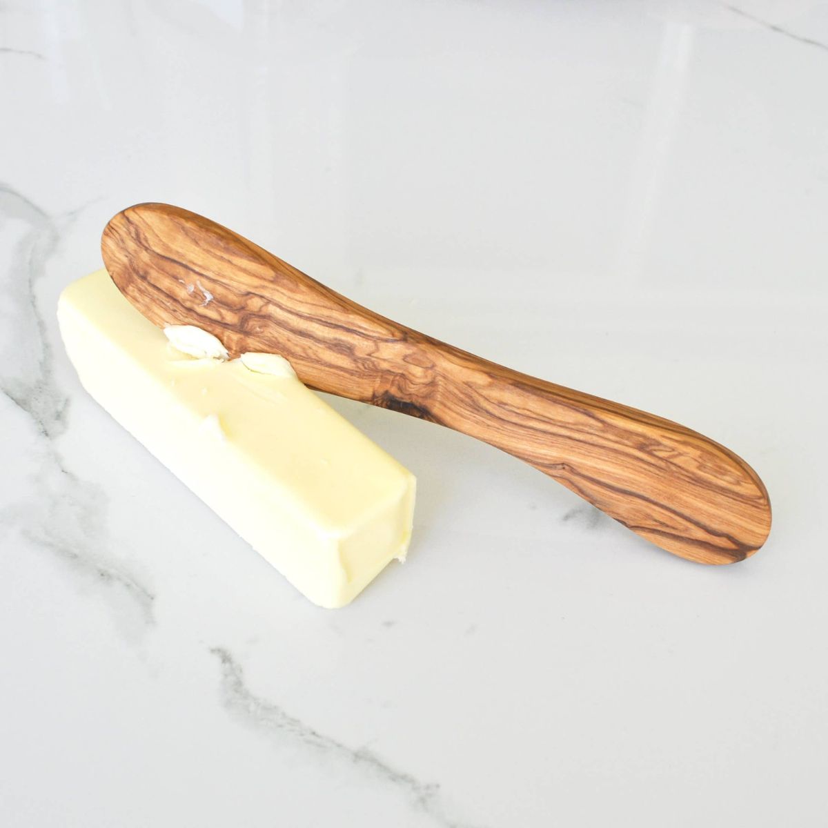 Wooden butter knife with a stick of butter on a marble surface