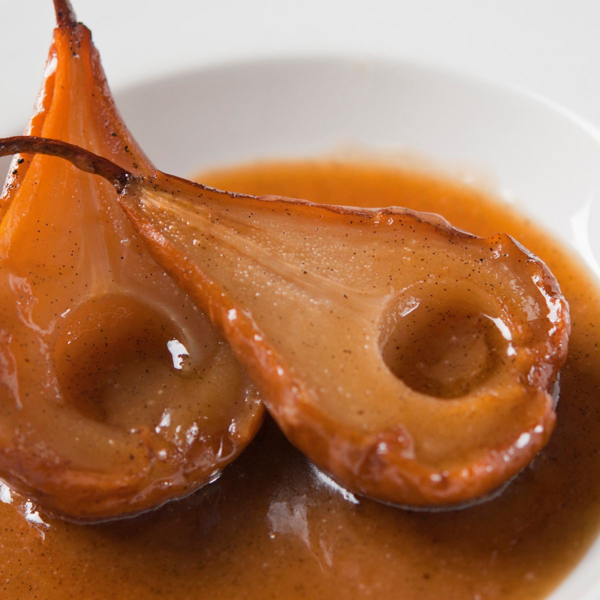 Two poached pears in a rich, brown sauce on a white plate.