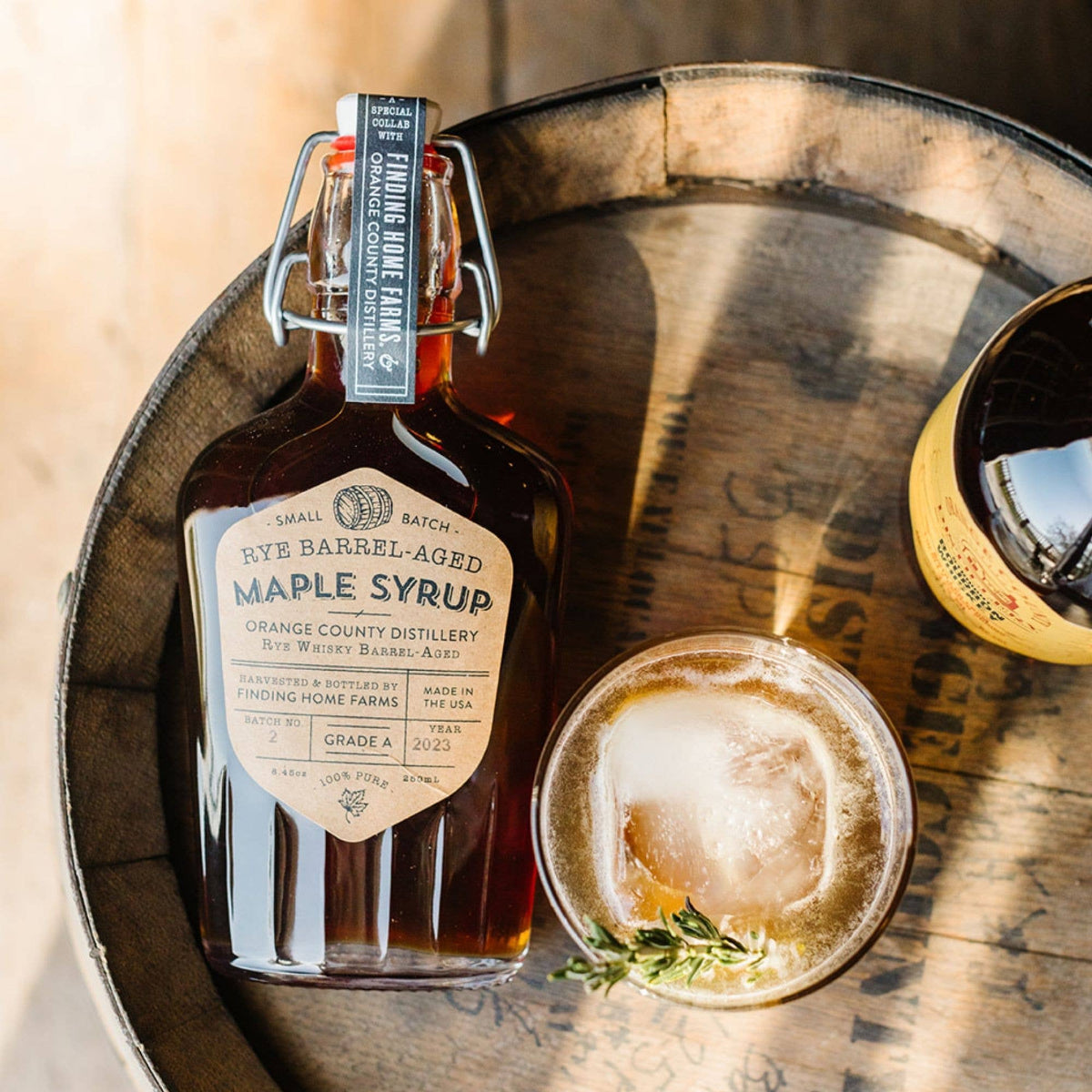 Bottle of rye barrel-aged maple syrup on a wooden surface with a glass of a beverage.