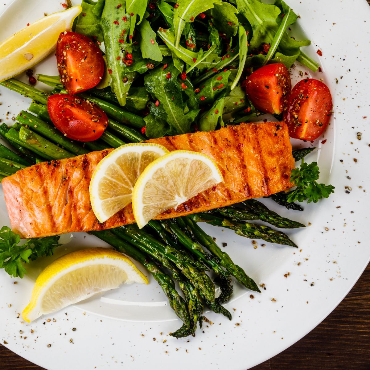 Salmon dish with asparagus, tomatoes, and lemon wedges on a white plate.