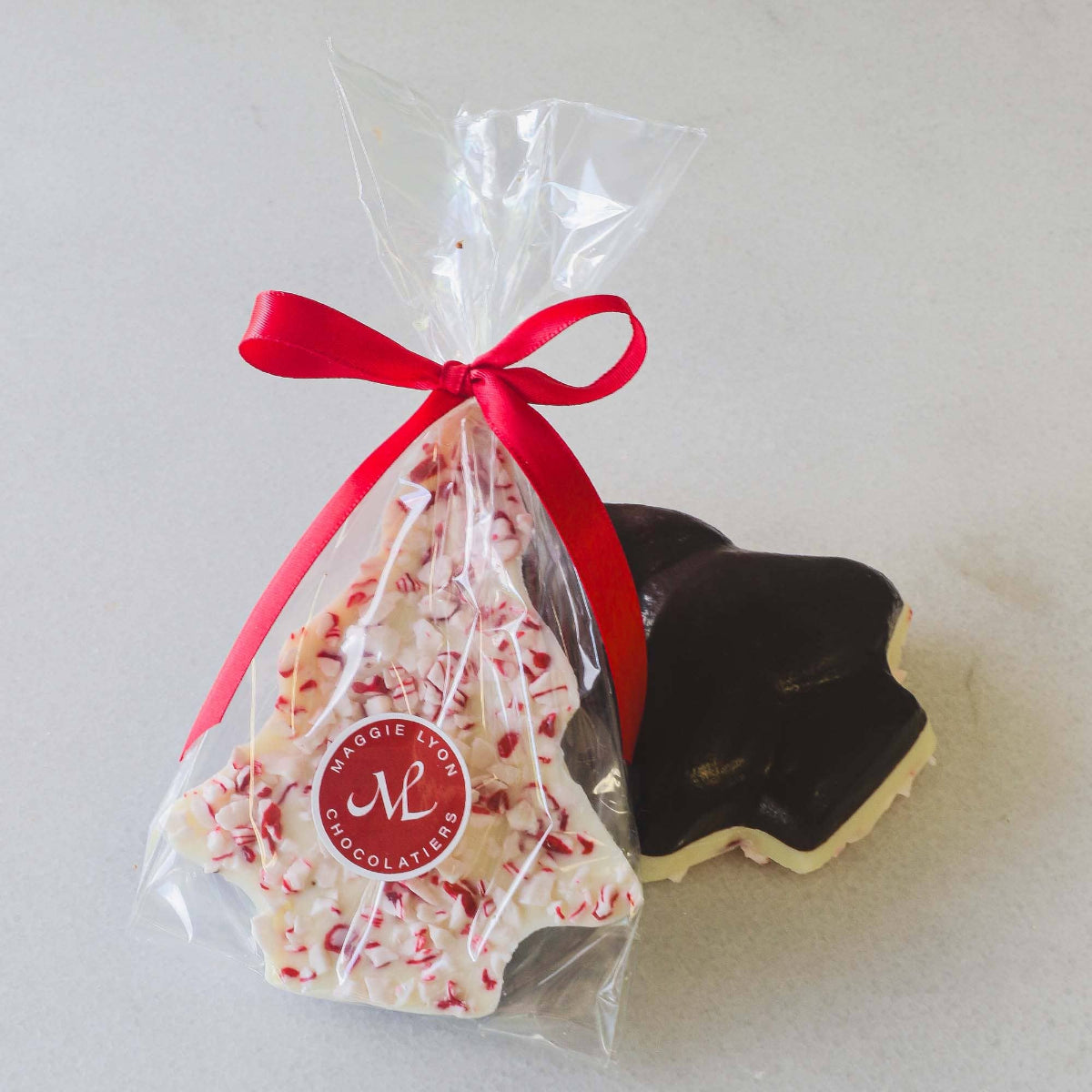 Chocolate cookies with peppermint candy in a clear bag tied with a red ribbon, branded &#39;Maggie Lyon Chocolatier&#39;.